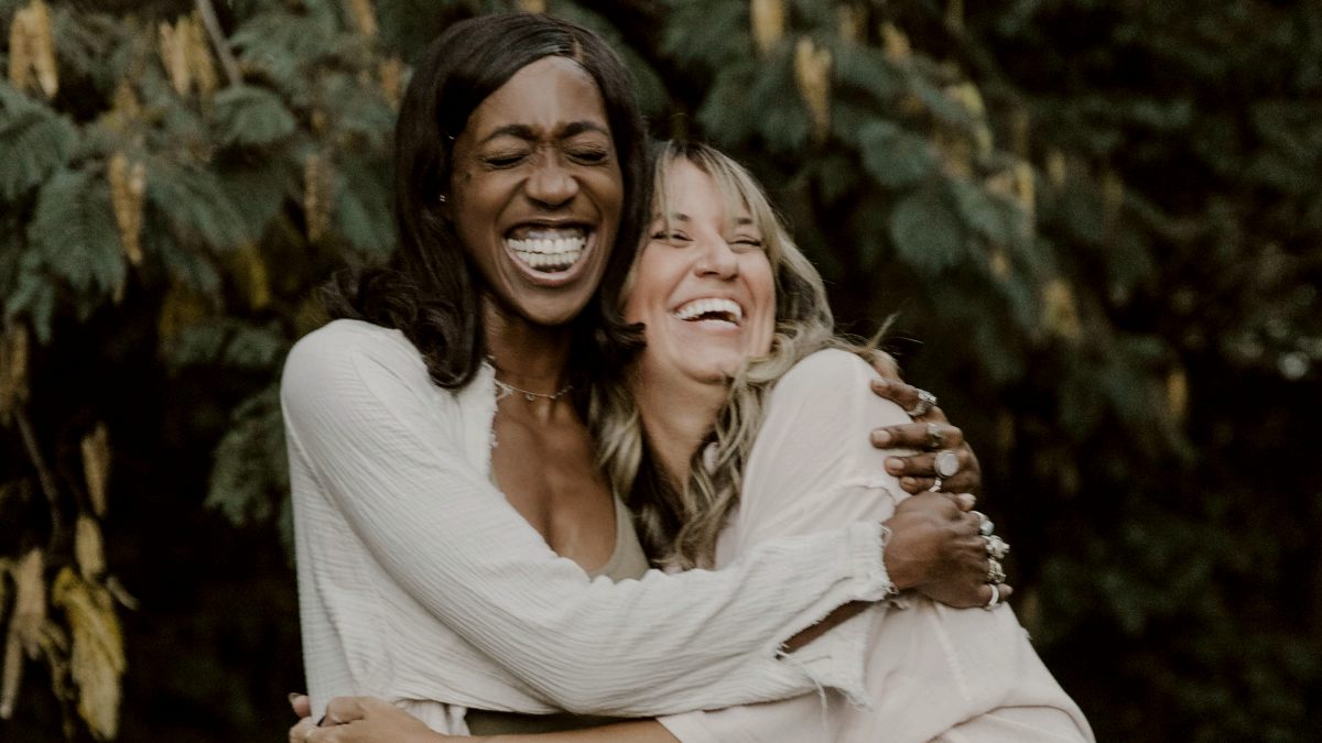 
two women hugging each other in front of trees
