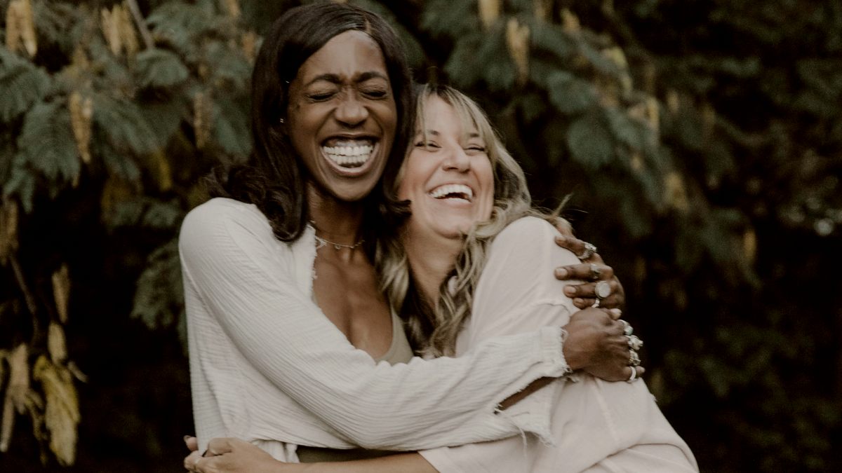 
two women wearing white hugging each other in front of trees during the day by tabitha turner
