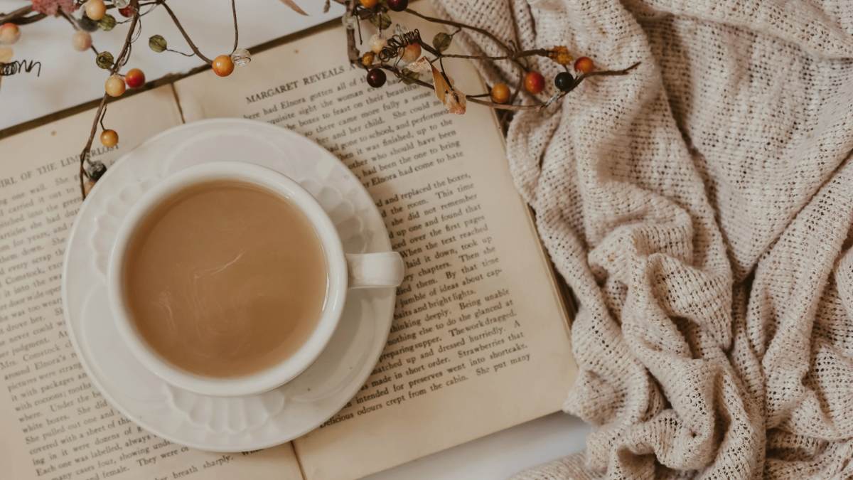 
white-ceramic-mug-on-white-book-next-to-a-cozy-blanket
