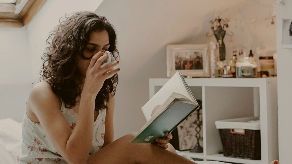 
woman-holding-book-and-drinking-tea-in-bed
