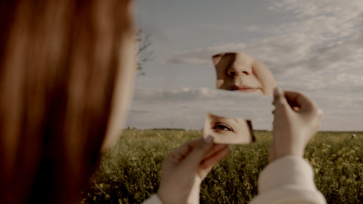 
Woman holds fragmented mirror reflecting parts of her face by Kateryna Hliznitsova
