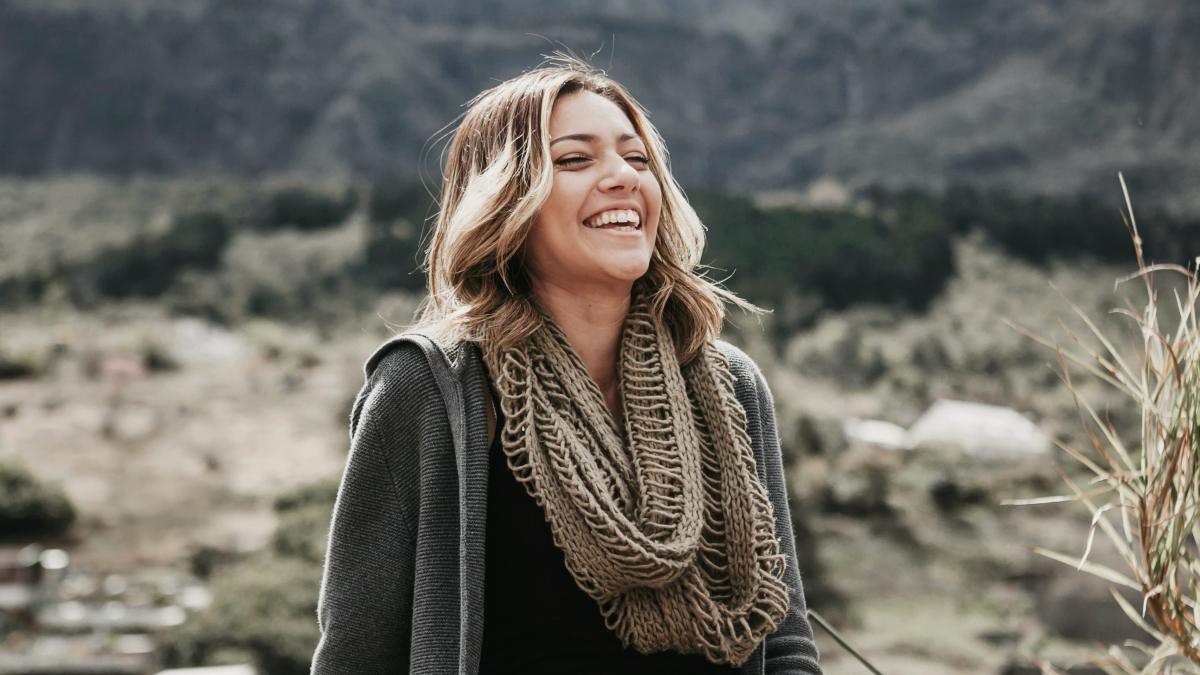 
woman in a scarf sitting near mountain range laughing
