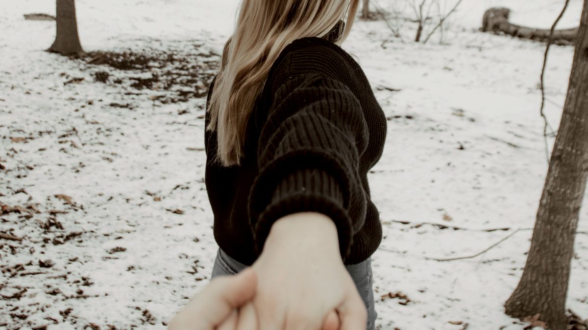 
woman in black sweater standing on snow covered ground leading her boyfriend
