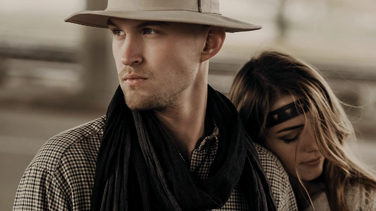 
woman in stylish boho clothes and white dress hugging handsome cowboy man in white hat and scarf
