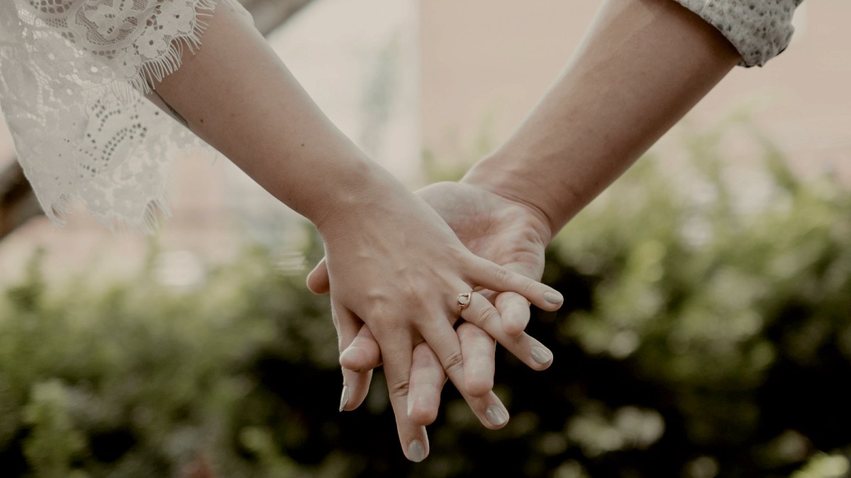 
woman in white lace wedding dress holding hands with her husband with her wedding ring showing by Isaac Iverson
