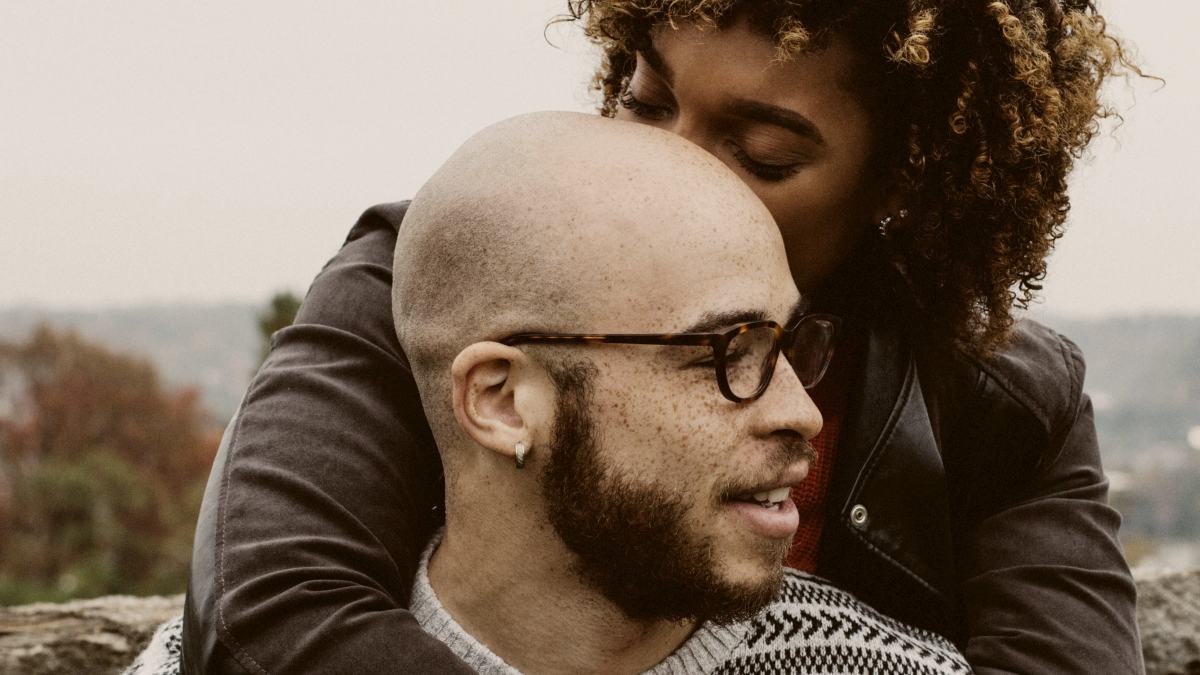 
woman kissing mans head embracing him from behind outside by justin follis
