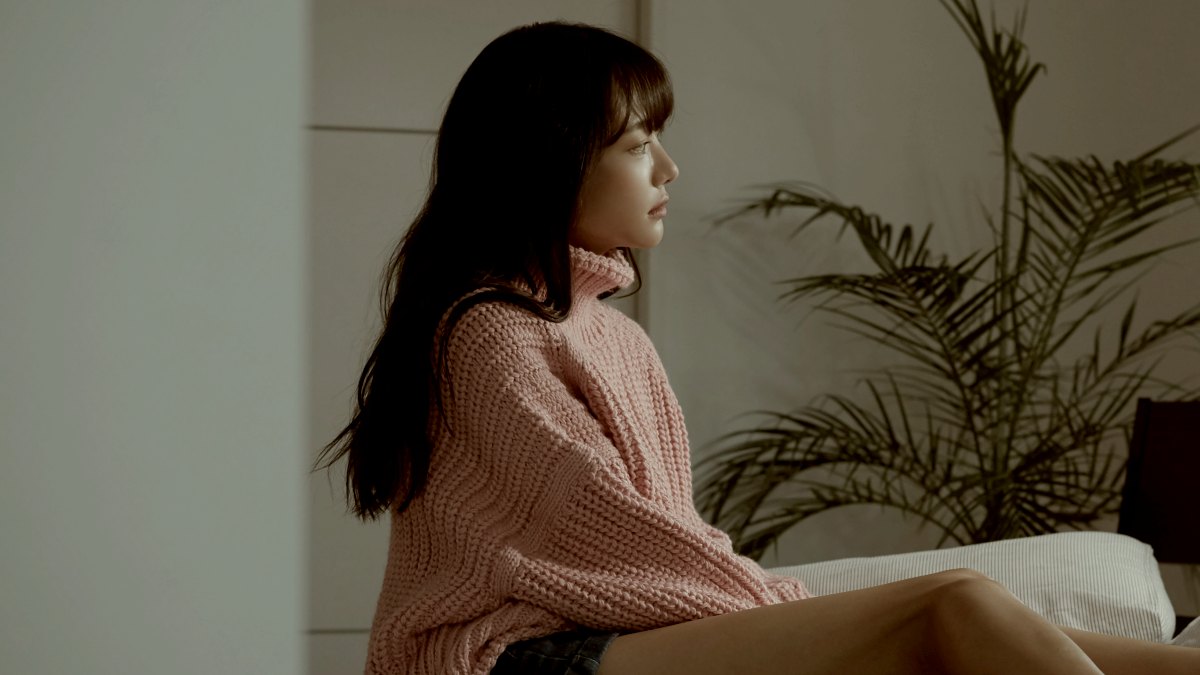 
woman on a bed in pink jersey with dark hair gazing out a window in the day time by getty images
