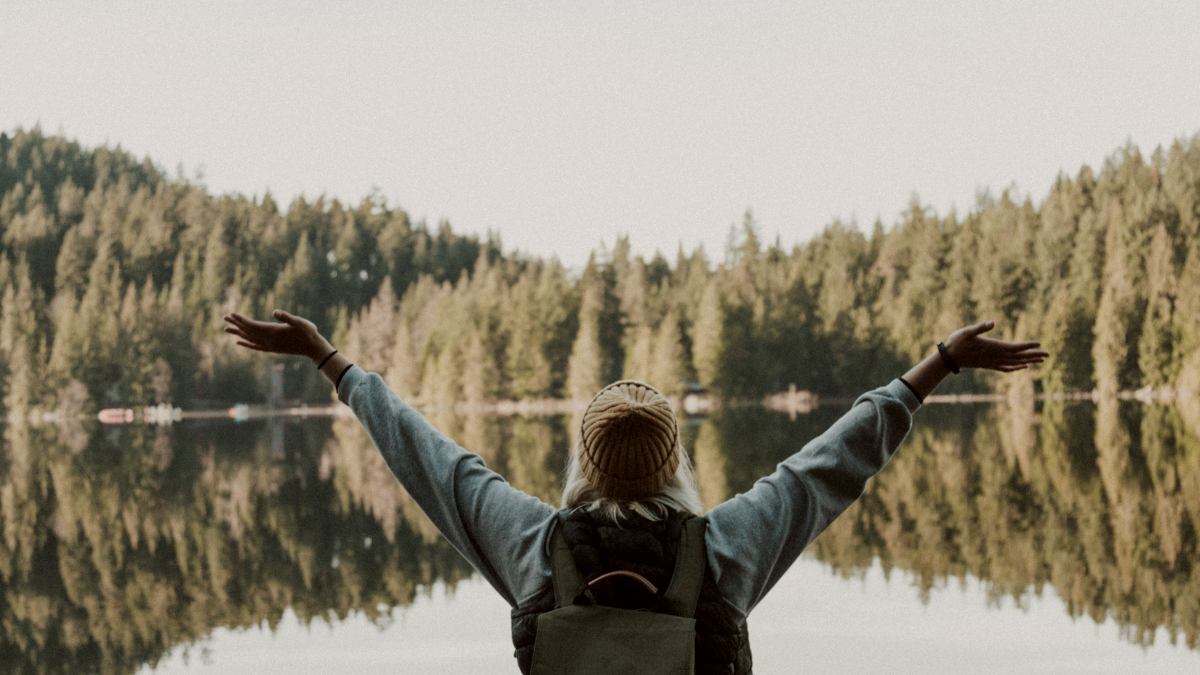 
woman open her arms facing calm body of water
