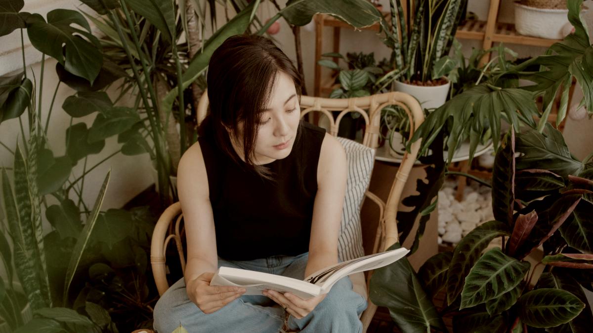 
Woman reading a book surrounded by lush green plants by Kailun Zhang
