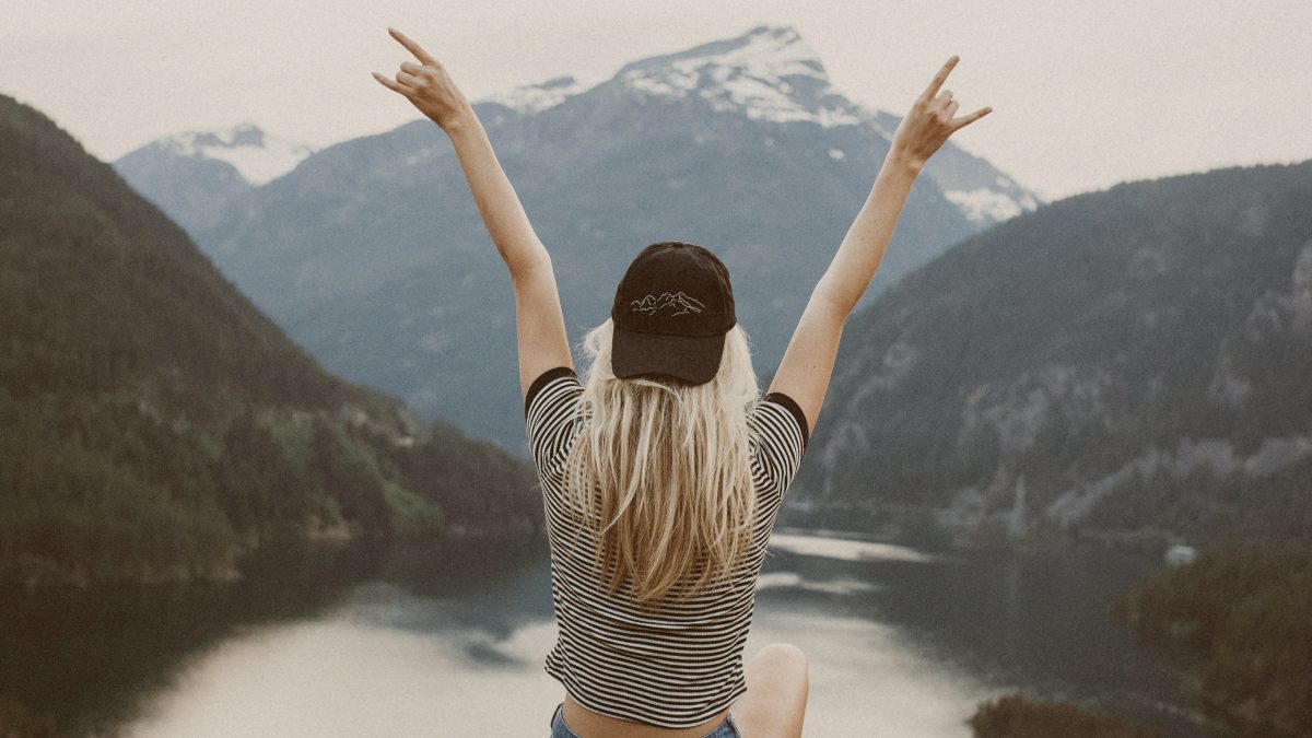 
woman sitting on cliff raising both hands by Becca Tapert
