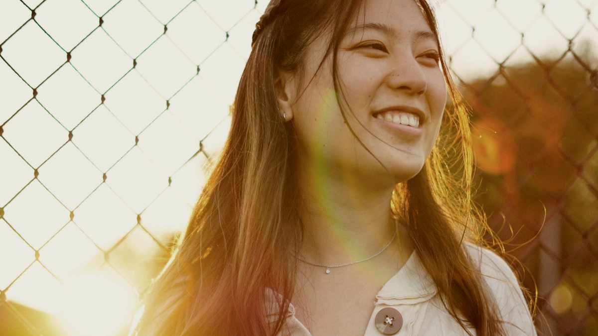 
woman smiling in front of chain link fence during golden hour
