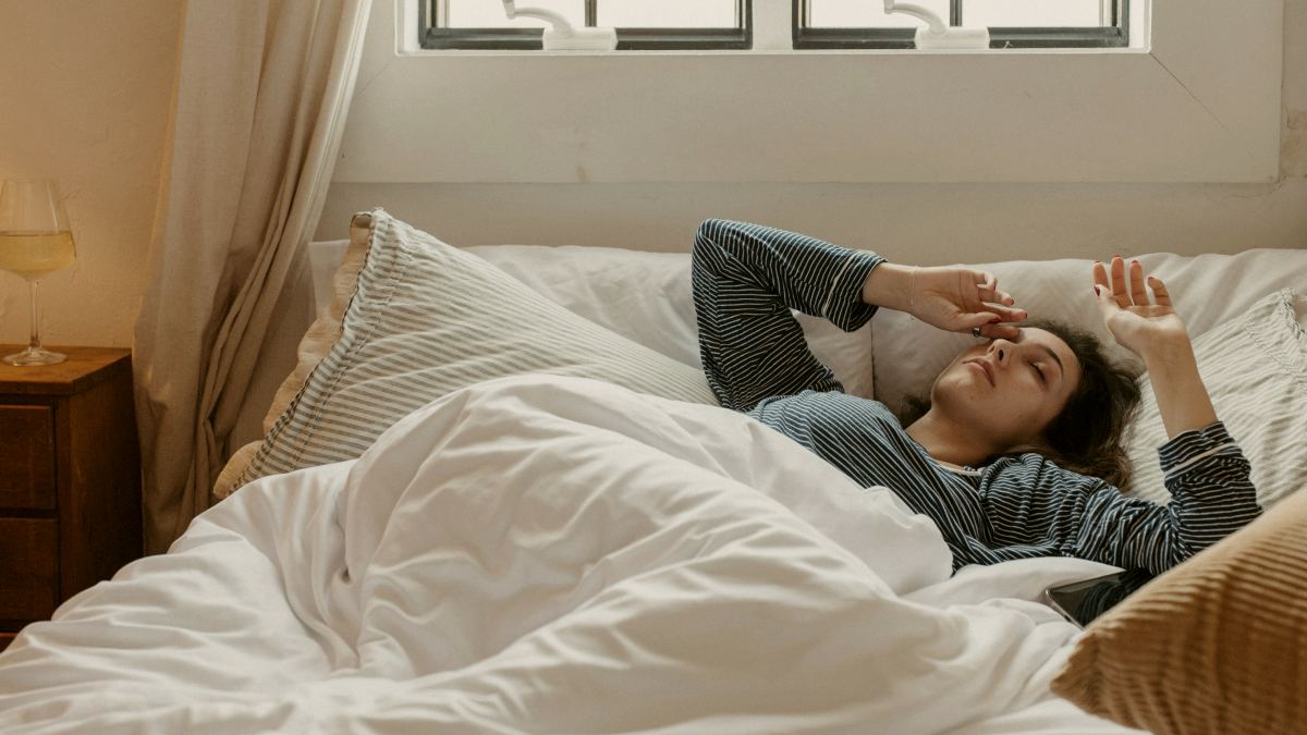 
Woman waking up in bed reaching for the sky with laptop on bed by Stephanie berbec
