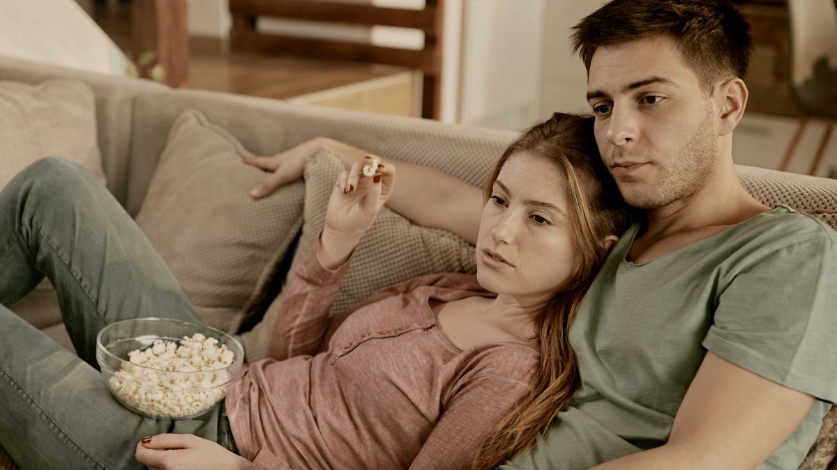 
Young couple eating popcorn while relaxing on the sofa and watching TV in the living room by Getty Images
