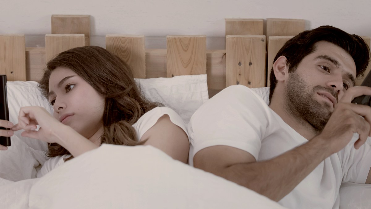
young couple in bed on cell phones ignoring each other by Getty Images
