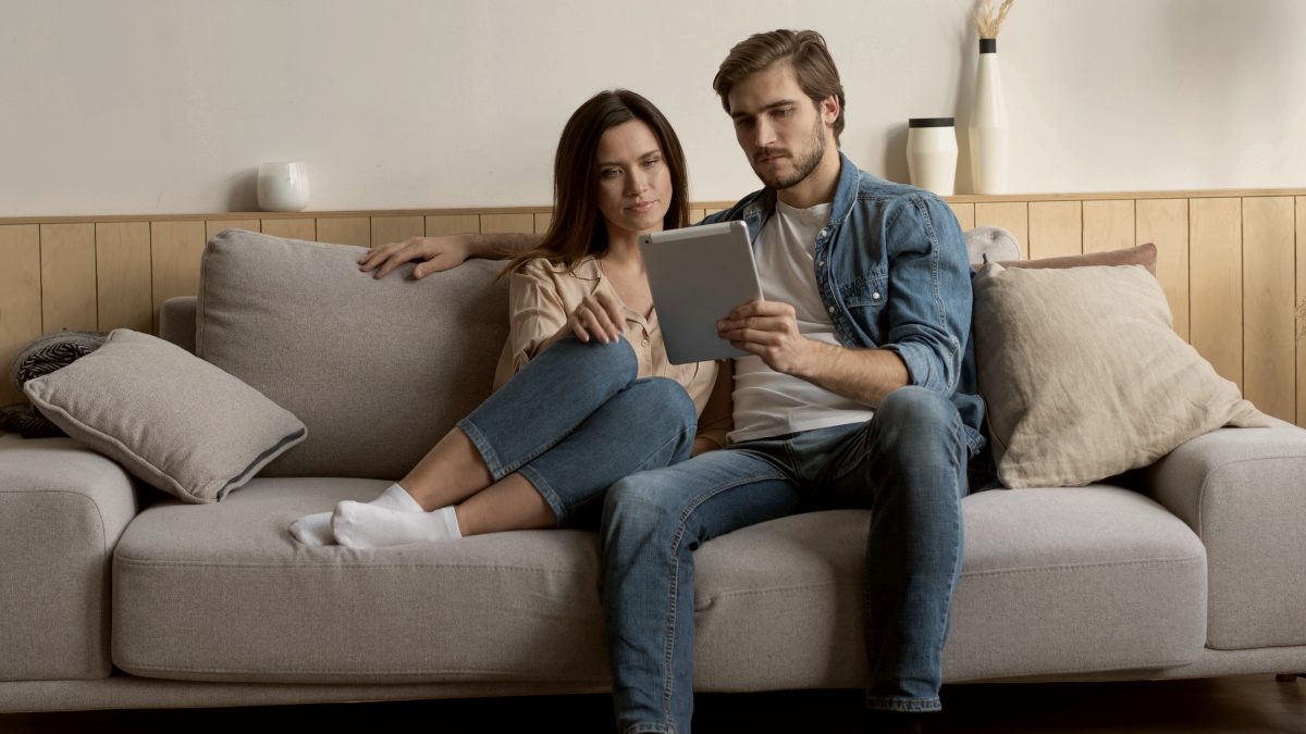 
Young couple sitting on couch at home using a tablet PC for Internet and social media
