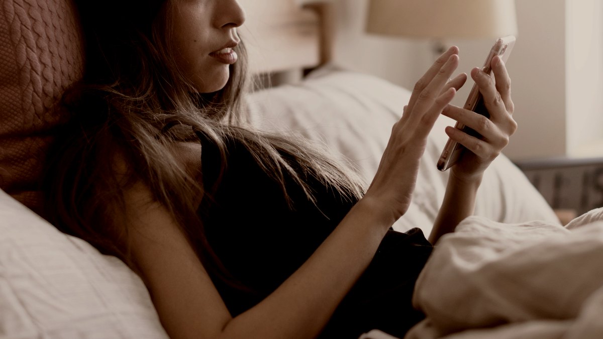 
young woman using pink iphone in bed by curated lifestyle
